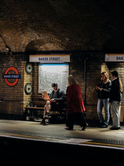 A section of a brick wall in a London underground station featuring a round London Underground sign with a red circle and a blue rectangular bar displaying the name 'BAKER STREET' in white capital let